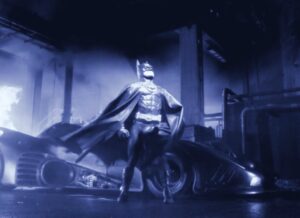 A screenshot of Michael Keaton in costume as Batman in Tim Burton’s Batman, edited with a blue color tint in the style of early colorized silent film.