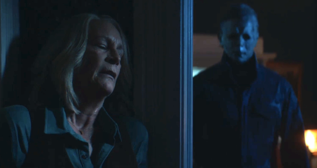 Laurie Strode hides behind a corner as Michael Myers approaches in Halloween Ends.