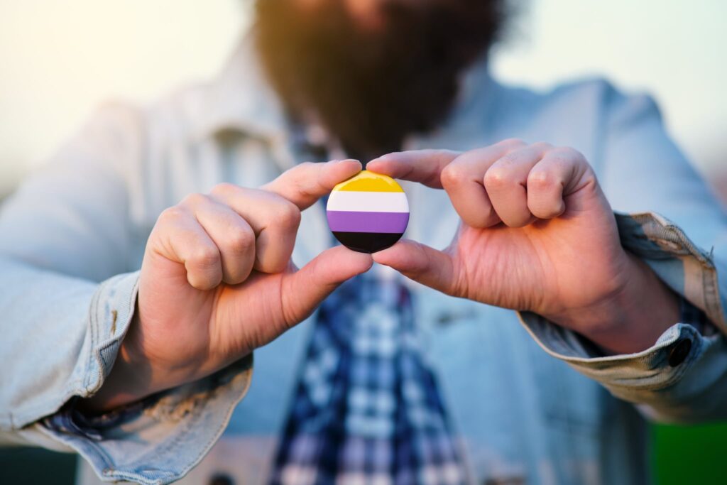 An unrecognizable person holding and showing a pin with non binary colors flag