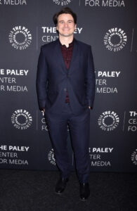 full body photo of Jason Ritter smiling in a black suit