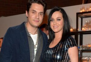 John Mayer (L) in gray top with blue jacket standing next to Katy Perry, who is wearing a black and silver top