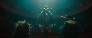 Namor descends into the depths of his throne room wearing an elaborate feathered crown with his arms outstretched in Black Panther: Wakanda Forever