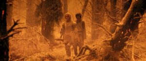 Galadriel and Theo walking through a post-erruption Southlands. They are mid-distance, and everything is filtered orange and there’s ash everywhere