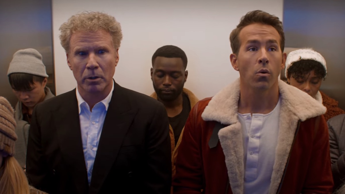 Will Ferrell in a black sports coat and Ryan Reyndols in a Santa Claus jacket on a full elevator of people in Spirited