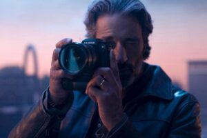 A man holding a Fujifilm X-H2S camera, eyeing up a shot during sundown.