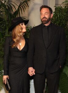Jennifer Lopez in a black dress and hat smiling. at Ben Affleck in a black suit