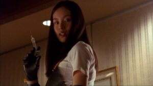 A woman in a white shirt with black gloves prepares a deadly syringe in Takashi Miike’s Audition