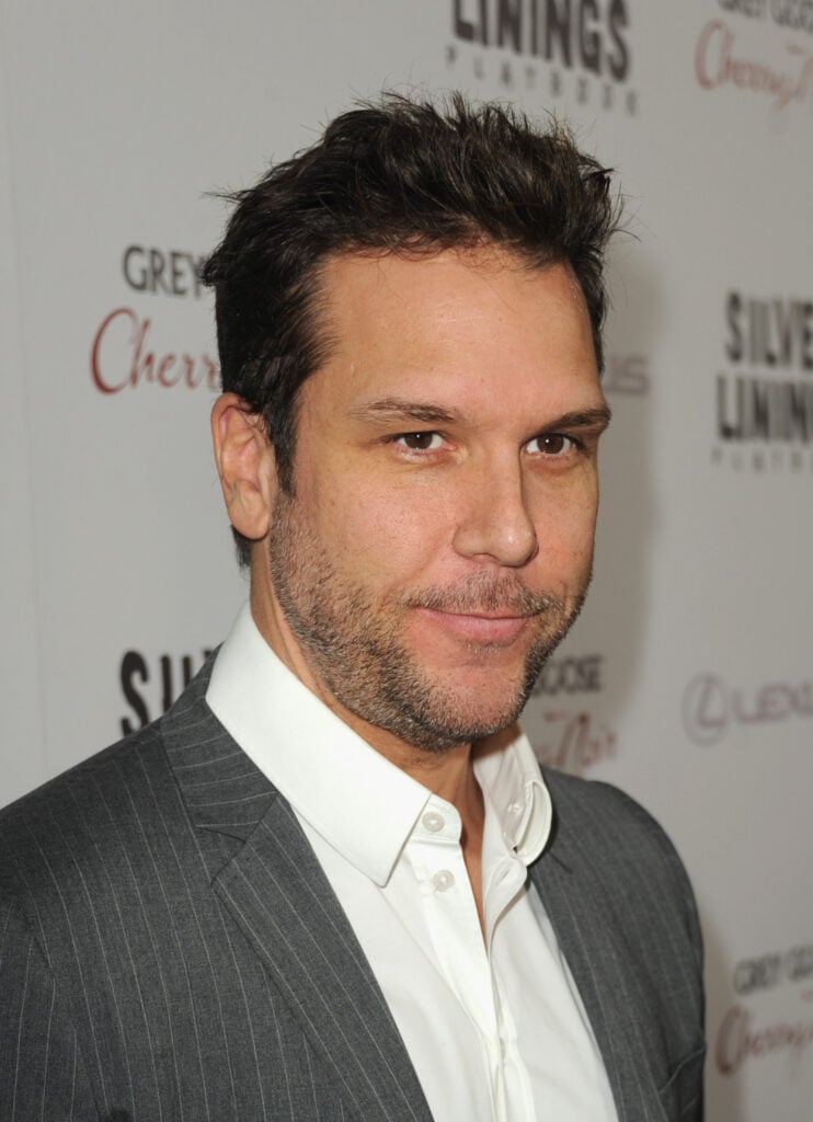 Dane Cook is seen from the chest up in gray pinstriped blazer over white dress shirt