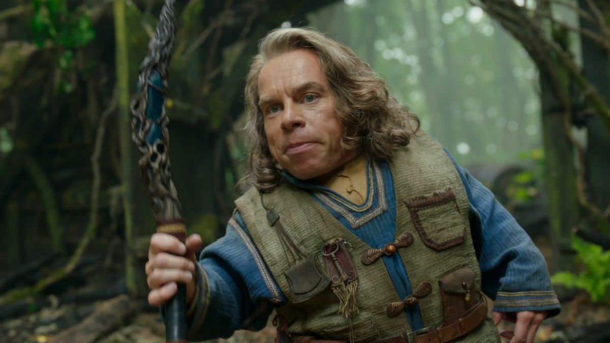 Warwick Davis as Willow, holding a large stick in the forest