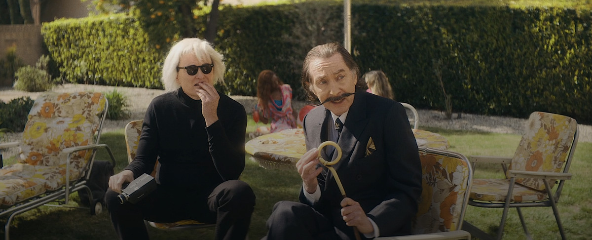 Conan O’Brien as Andy Warhol and Emo Philips as Salvador Dalí sit in flower-patterned lawn chairs and stare offscreen in Weird: The Al Yankovic Story