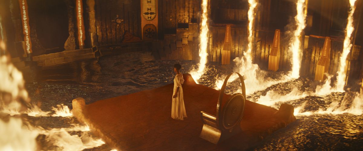 Shuri (Letitia Wright) stands in a throne room surrounded by pillars of fire reflected against pools of water in Black Panther: Wakanda Forever.