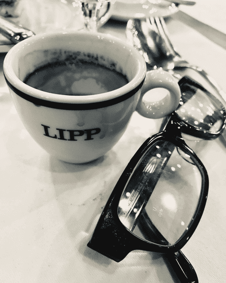A black and white image of an espresso and a pair of glasses on a cafe table