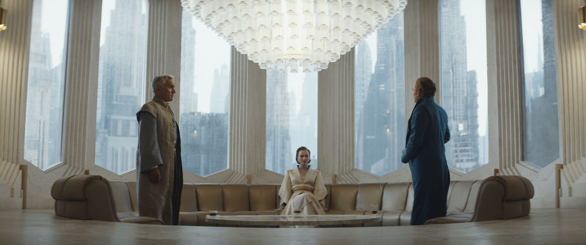 Mon Mothma sits in her large, recessed couch perfectly in the center of a the frame as two others stand at either end, addressing her.