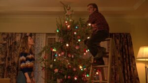 A man on a ladder decorates a Christmas tree as a woman watches in the movie "A Christmas Story Christmas."