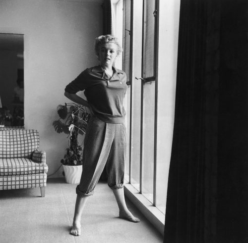 Marilyn Monroe photographed posing near a window in a sweater and checkered pants circa 1955