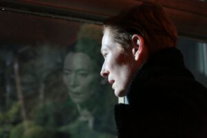 A woman in a black jacket looks out a window