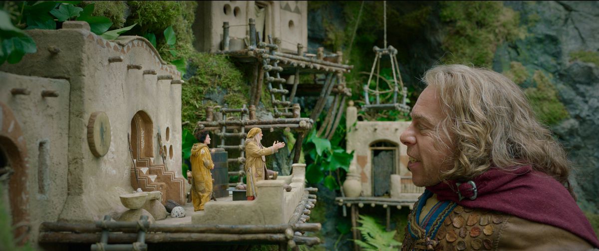 (L-R): Ganush (Amalia Vitale), Rool (Kevin Pollak) and Willow Ufgood (Warwick Davis) in Willow. Ganush and Rool, fairy-sized beings, stand on their miniature front porch to chat with Willow. 
