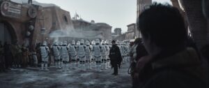 A young Cassian looks over as hordes of Stormtroopers march through the streets of Ferrix