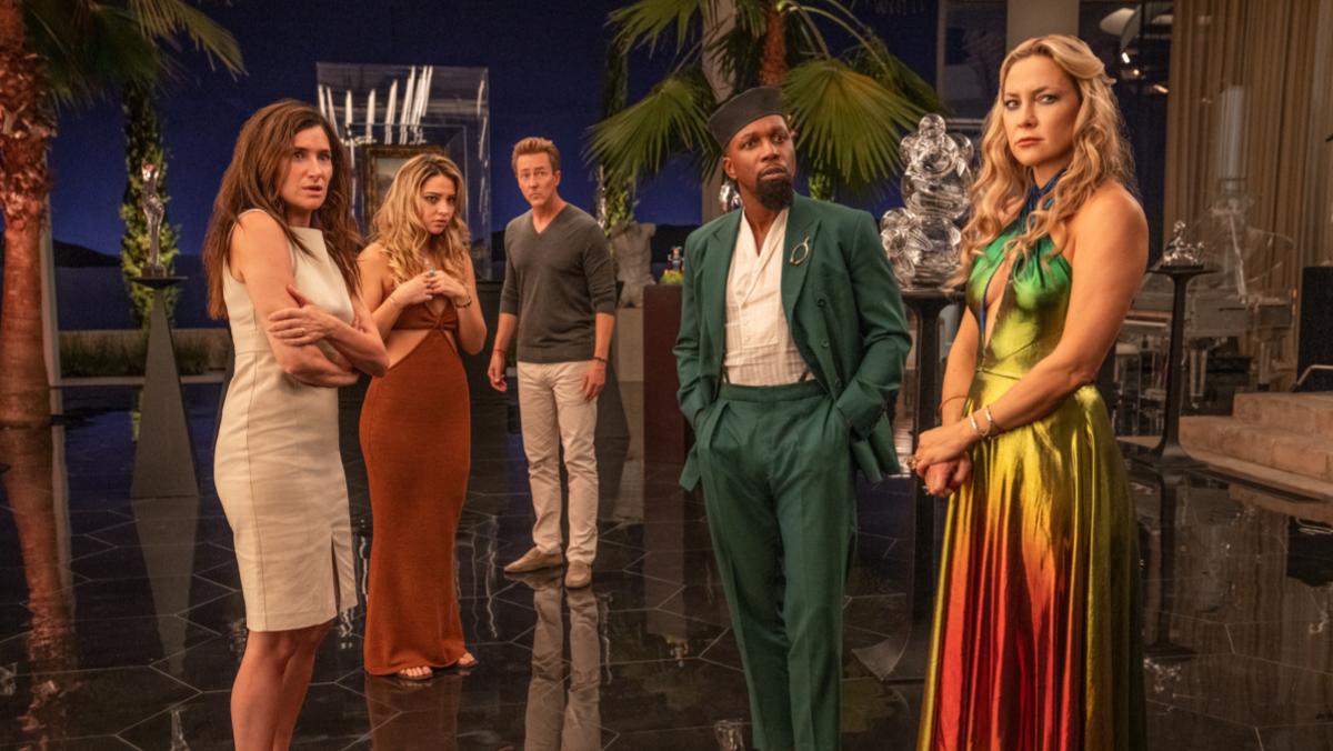 A still from Rian Johnson's new Knives Out movie Glass Onion shows the cast including Kathryn Hahn, Leslie Odom Jr., Kate Hudson, and Edward Norton