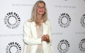 Jan Smithers smiles in cream-colored jacket against white backdrop