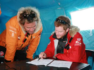 2013 photo of Dominic West in an arctic coat looking over papers with Prince Harry in a similar coat
