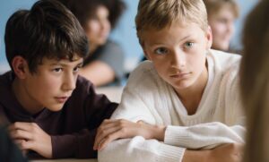 Two boys in sweaters listen to someone talking in a scene from "Close."