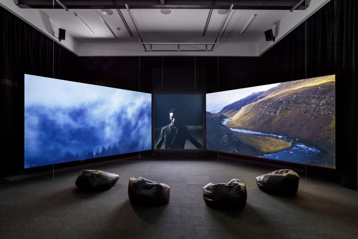 Three screens, the left and right screen show mountains and the center screens shows a man with arms by his side