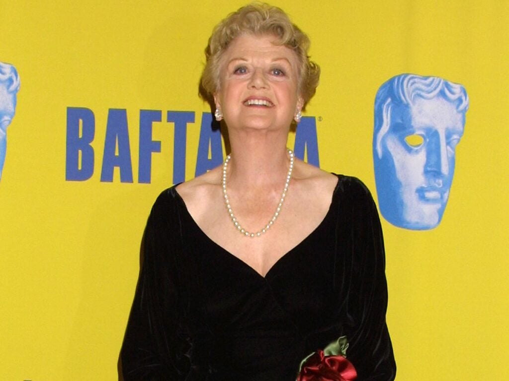 Angela Lansbury looking up and smiling in front of a yellow background