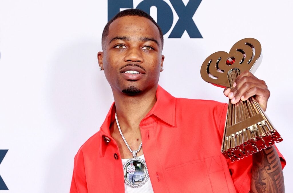 Roddy Ricch wearing a red shirt and posing with his iHeartRadio Music Award.