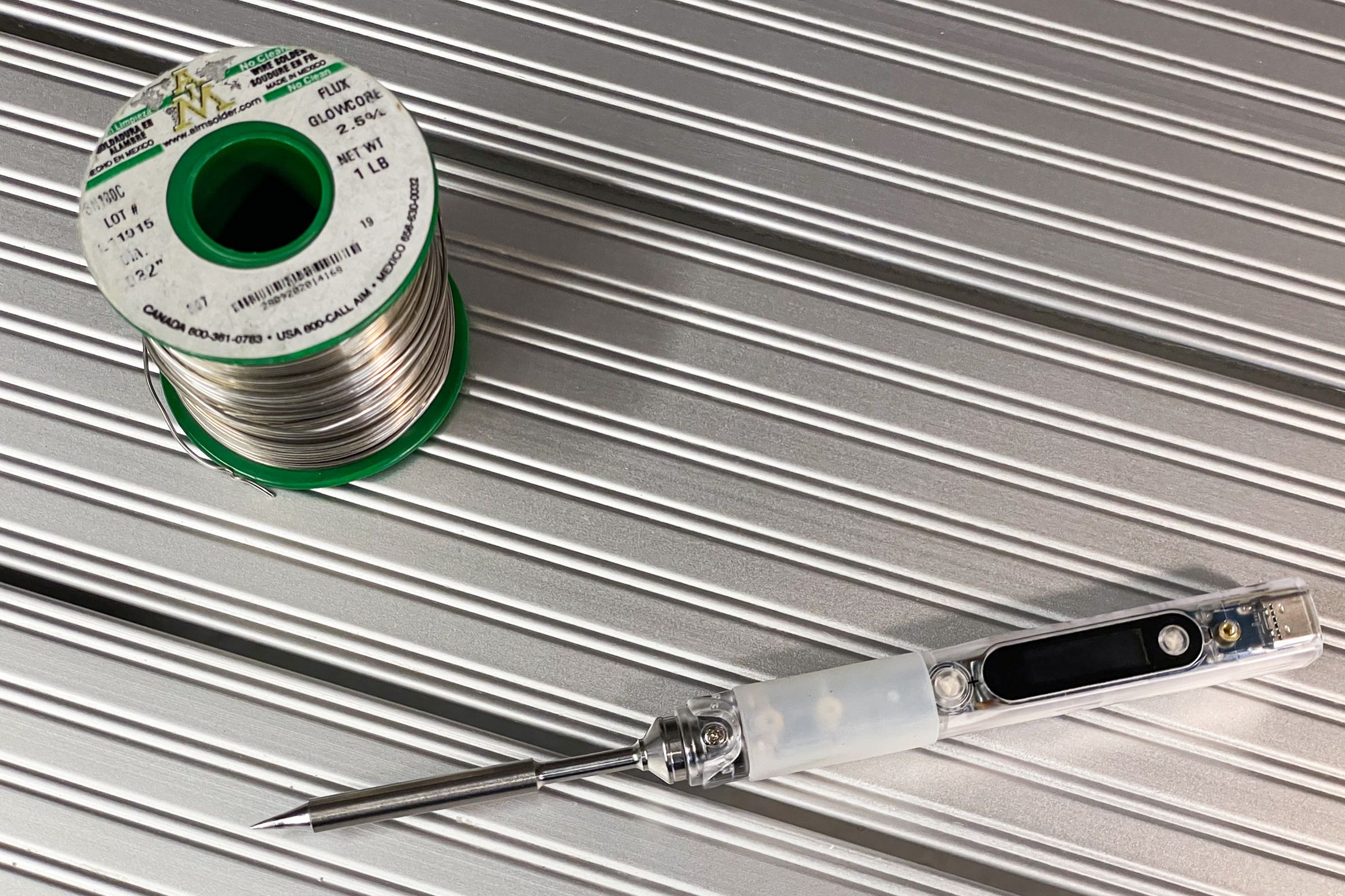 A pinecil in a clear case next to a spool of SN100c Solder.