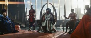 A woman sits on a futuristic-looking throne flanked by guards in a scene from "Black Panther: Wakanda Forever."