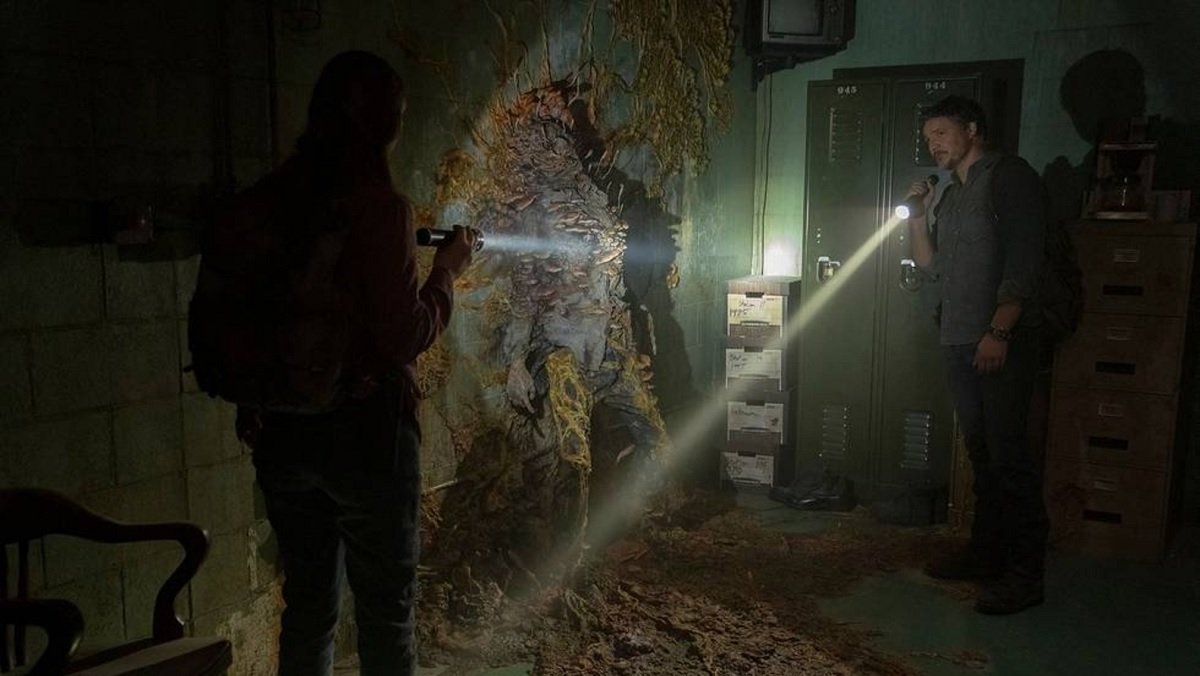 Joel (Pedro Pascal) and Tess (Anna Torv) shine flashlights on a human fungal growth in a dark, abandoned office building in the first episode of The Last of Us.