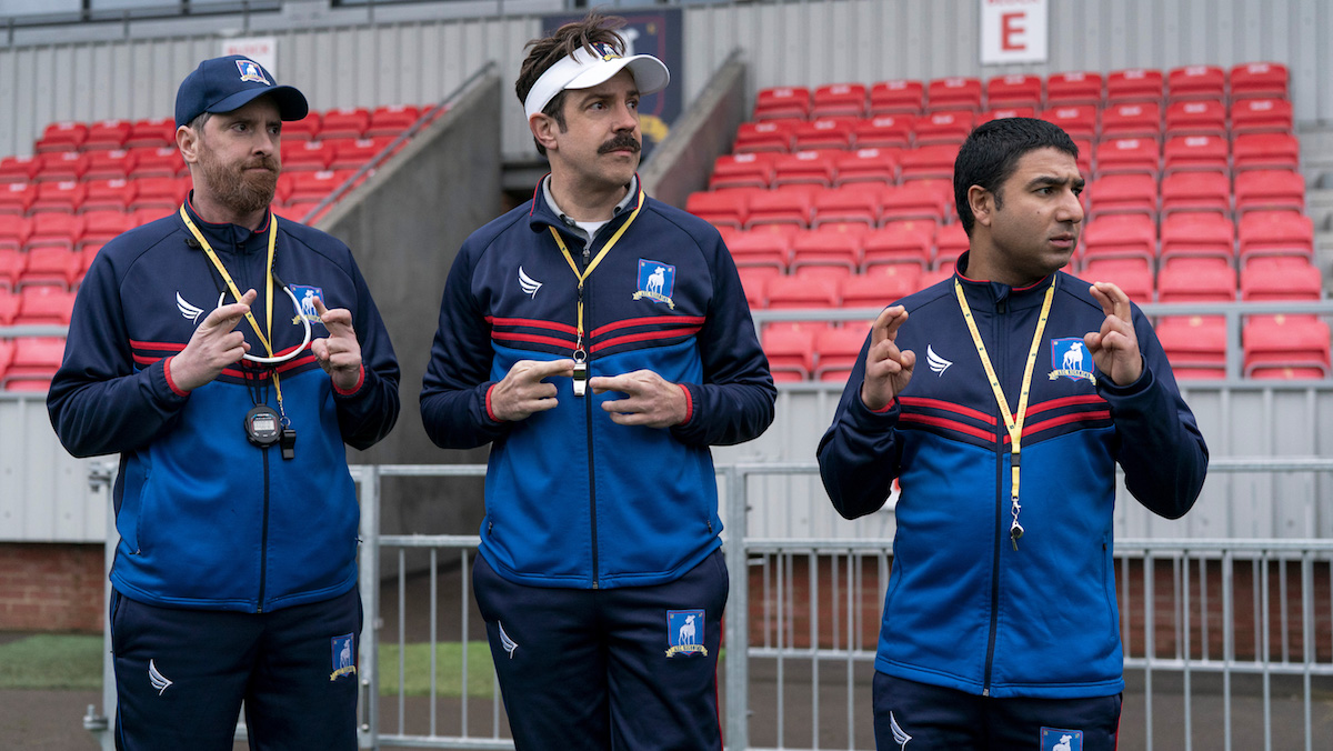 Three men in coaching uniforms cross their fingers