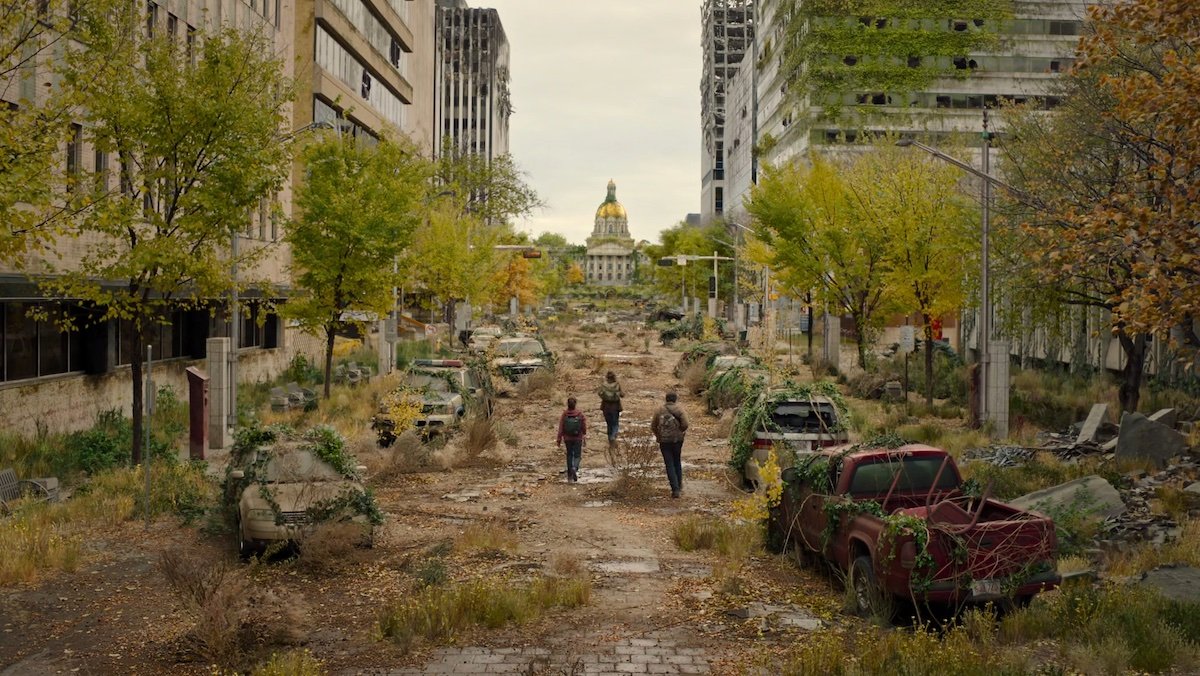 Joel, Tess, and Ellie walk down a ruined street in Boston to a fictional version of the Massachusetts State House on The Last of Us