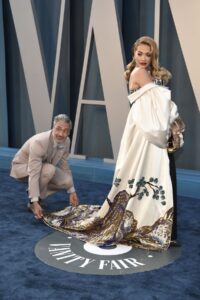 A man kneels down to adjust the train of a woman's evening gown
