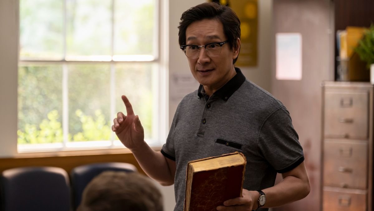 Ke Huy Quan standing  in a classroom holding a book in american born chinese
