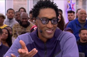 Scottie Pippen during an appeance on ESPN holding his hands up and wearing a purple jacket.
