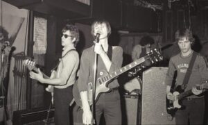 Black and white shot of the band on stage with Verlaine singing