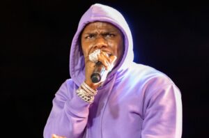 DaBaby wearing a purple hoodie while performing with a microphone in his hand.