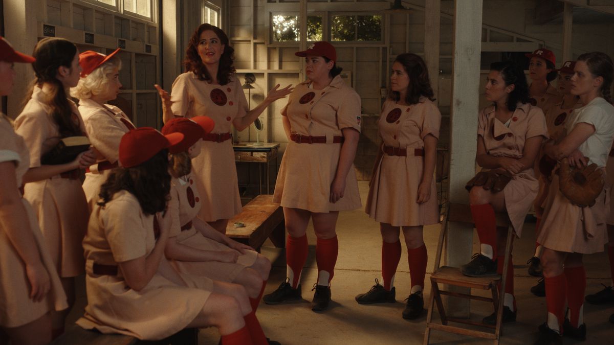 Greta (D’Arcy Carden) standing and talking to the assembled Rockford Peaches team in the locker room