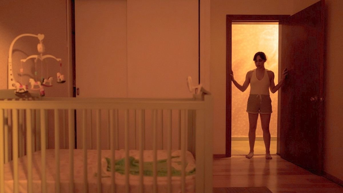 a woman stands in front of a open door and looks at an empty crib in huesera movie