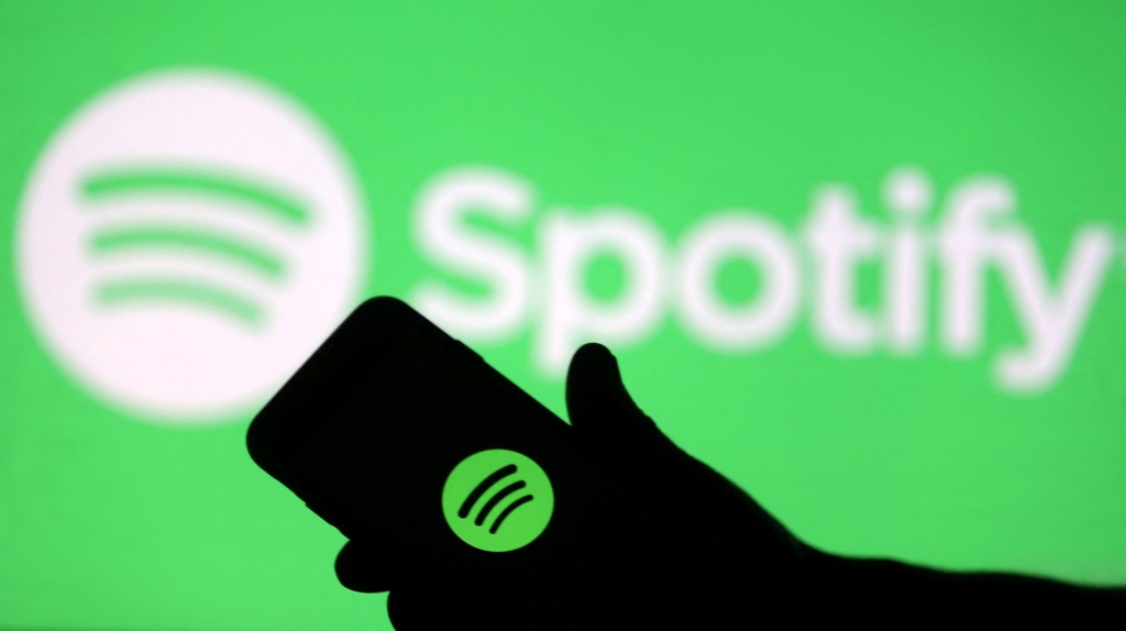A silhouette of a hand holding a phone with the Spotify logo.