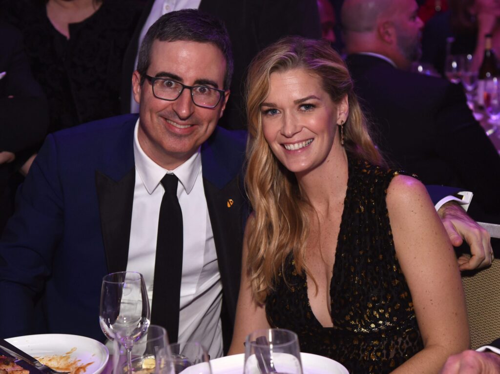John Oliver (L) and Kate Norley sitting at a table and smiling