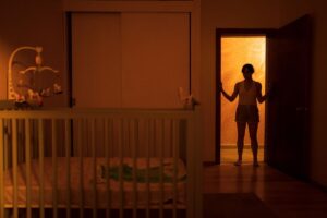 A silhouette of a woman stands in the doorway of a nursery illuminated from behind in the horror movie Huesera: The Bone Woman