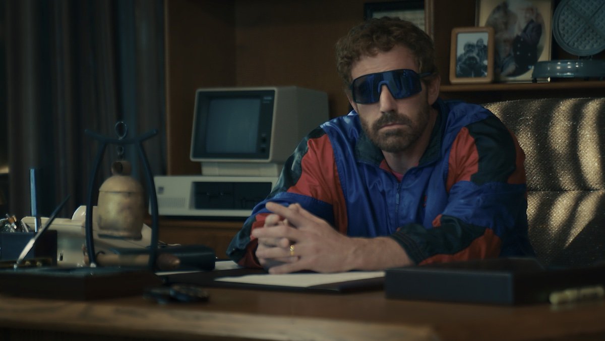 Ben Affleck as Nike CEO Phil Knight sits at his desk in a track suit with sunglasses in Air