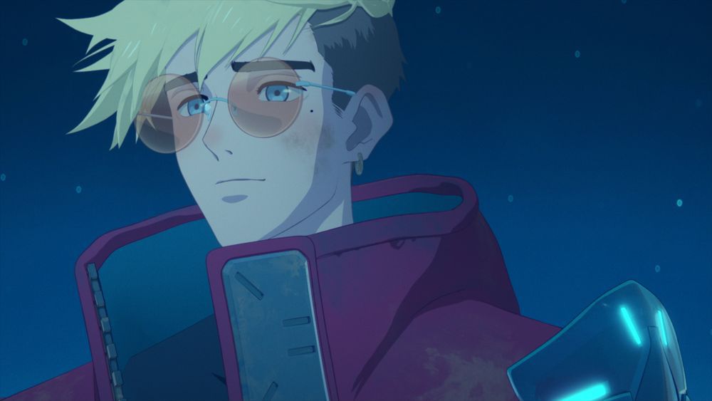 A yellow-haired anime man (Vash the Stampede) in a red coat with orange circular glasses smiling and staring off into the distance.