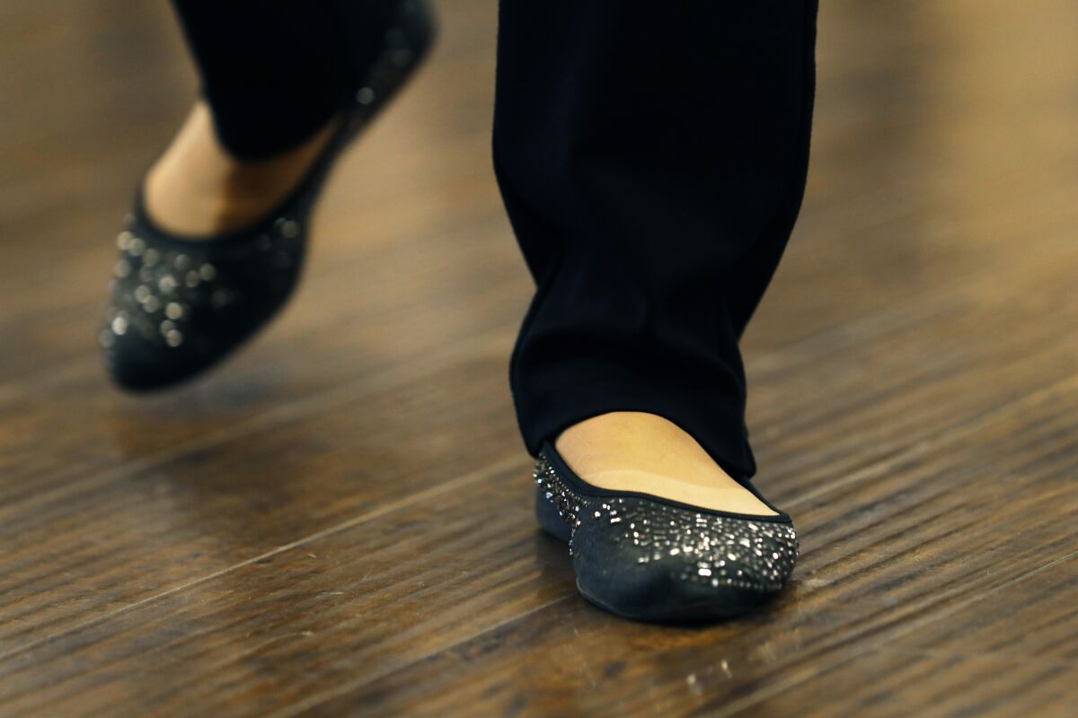 A view of two feet in black bedazzled ballerina shoes