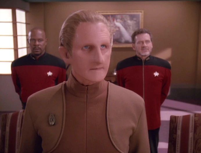 Constable Odo, a member of the Changling race in Star Trek: Deep Space 9. He is flanked by Captain Sisko on one side and a Starfleet admiral on the other. 