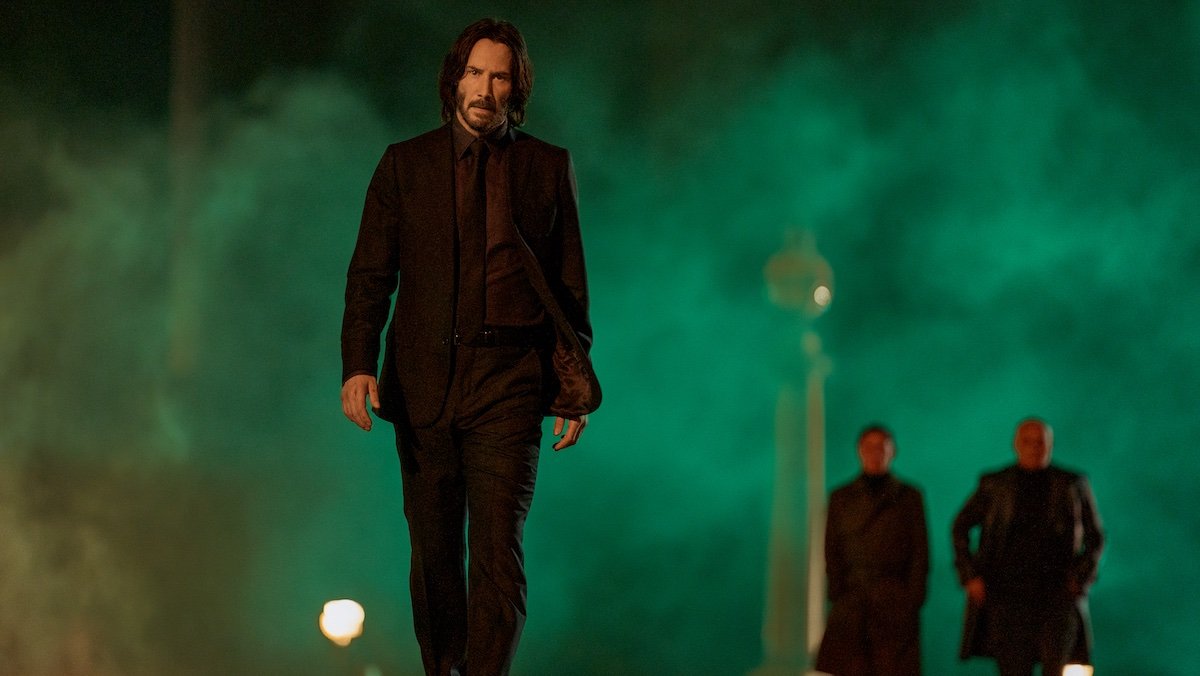 Keanu Reeves walks away from two men and a smoky green sky in John Wick: Chapter 4