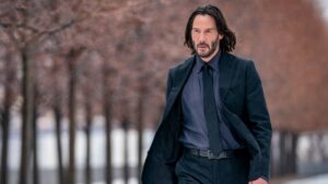 Keanu Reeves' John Wick in a black suit and long hair walks down a road lined with trees in Chapter 4